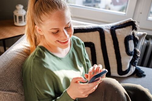 Woman sitting on a couch scrolling on social media. 